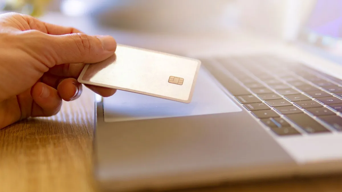 Person at a kitchen table calculating a credit card balance with statements and a calculator